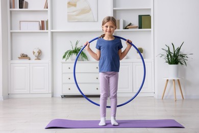 Photo of Cute little girl exercising with hula hoop indoors