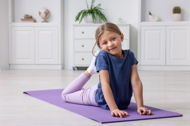 Photo of Cute little girl exercising on fitness mat indoors, space for text