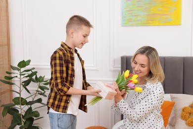 Photo of Happy Mother's Day. Son surprising his mom with gift and flowers at home