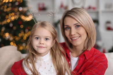 Photo of Cute little girl with her mom on sofa against Christmas lights