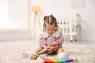 Photo of Cute little girl playing with toy guitar on floor at home