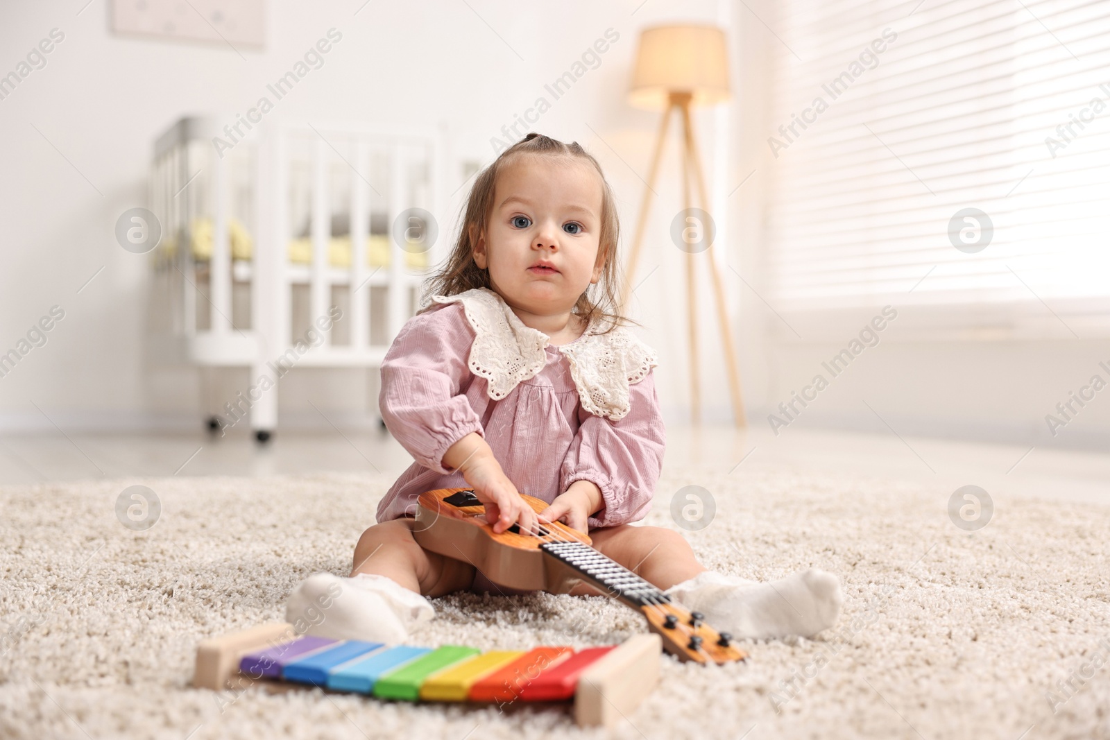 Photo of Cute little girl playing with toy guitar on floor at home