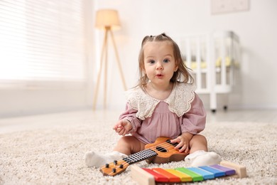 Photo of Cute little girl playing with toy guitar on floor at home, space for text