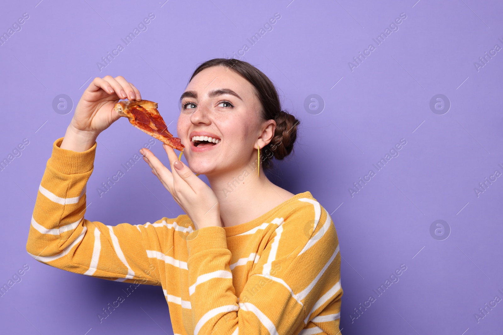 Photo of Beautiful woman with piece of delicious pizza on violet background, space for text