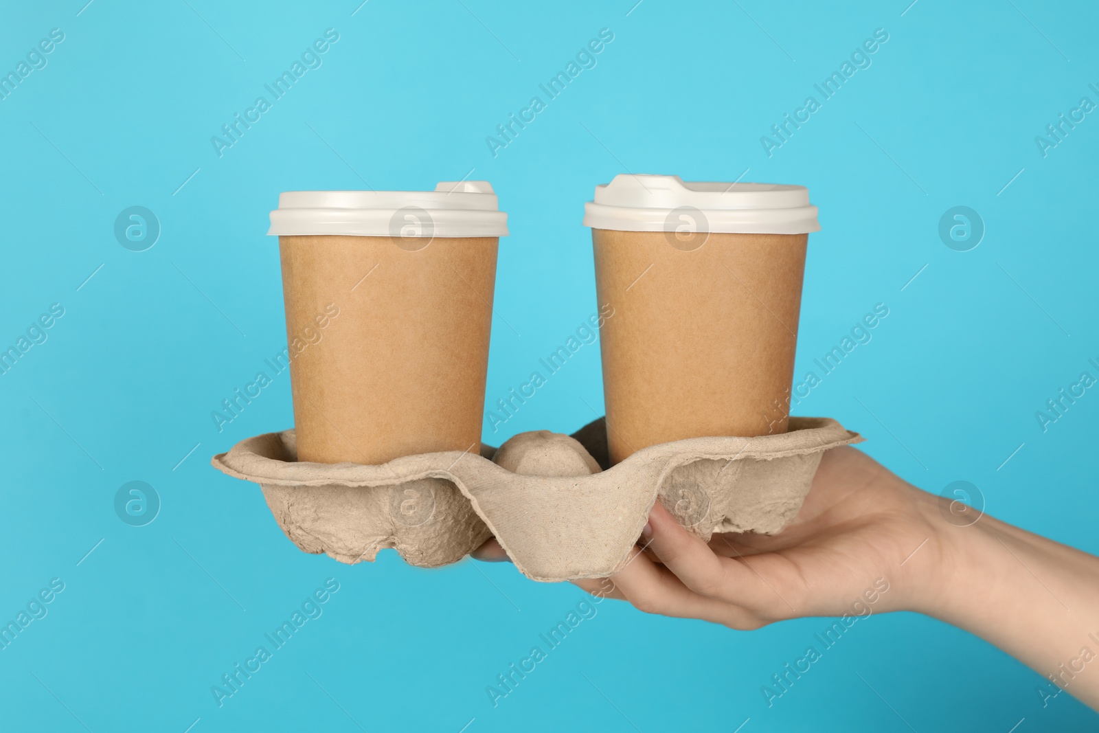 Photo of Woman holding holder with paper cups against light blue background, closeup. Mockup for design