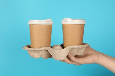 Photo of Woman holding holder with paper cups against light blue background, closeup. Mockup for design