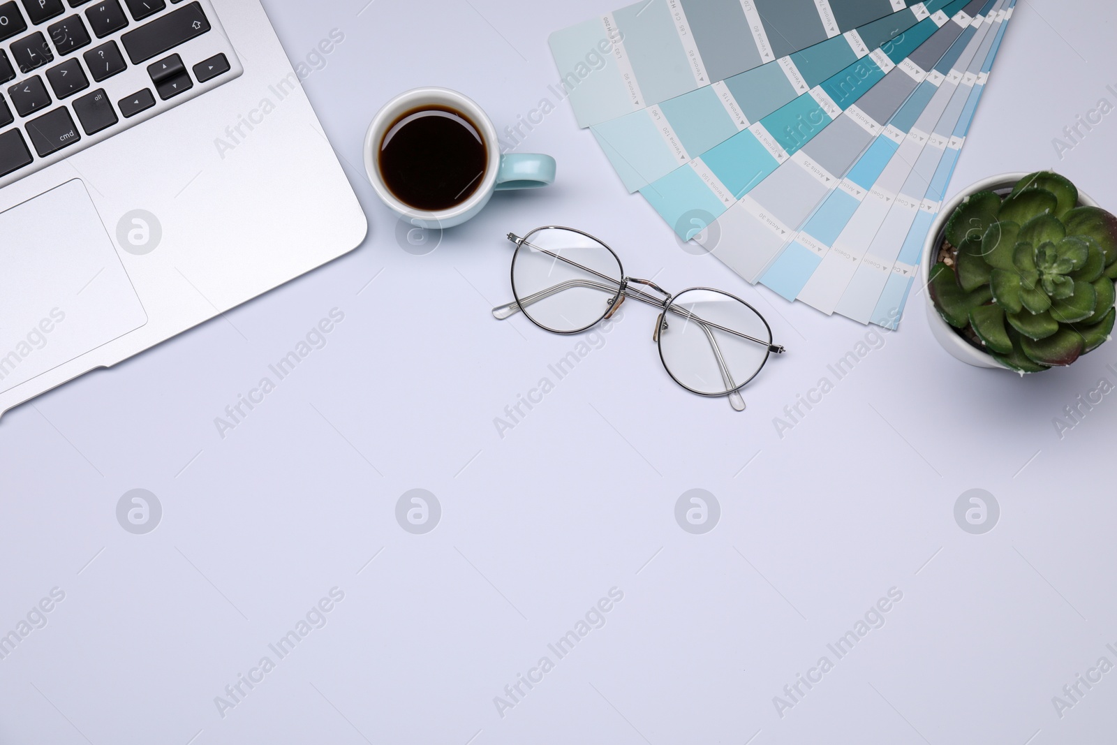 Photo of Designer's workplace with color palettes, cup of coffee, glasses and laptop on grey table, flat lay. Space for text