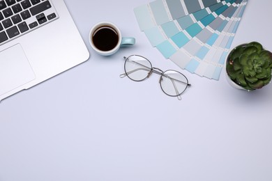 Photo of Designer's workplace with color palettes, cup of coffee, glasses and laptop on grey table, flat lay. Space for text