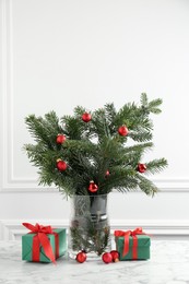 Photo of Beautiful decorated fir tree branches and Christmas gifts on table near white wall