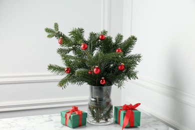 Photo of Beautiful decorated fir tree branches and Christmas gifts on table near white wall