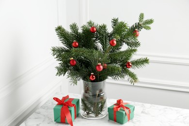 Photo of Beautiful decorated fir tree branches and Christmas gifts on table near white wall