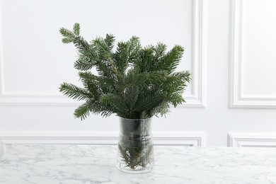 Photo of Beautiful fir tree branches on table near white wall. Christmas decor