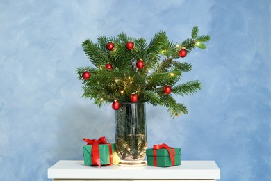 Photo of Beautiful decorated fir tree branches and Christmas gifts on table near blue wall