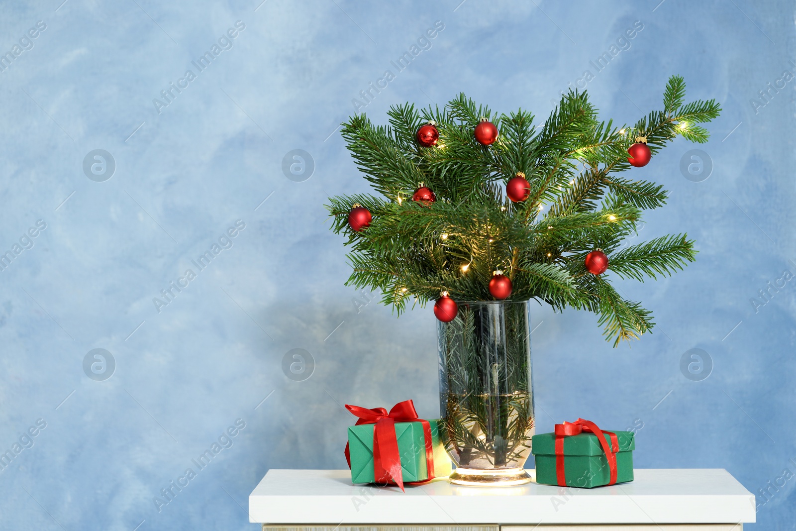 Photo of Beautiful decorated fir tree branches and Christmas gifts on table near blue wall