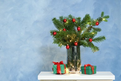 Photo of Beautiful decorated fir tree branches and Christmas gifts on table near blue wall