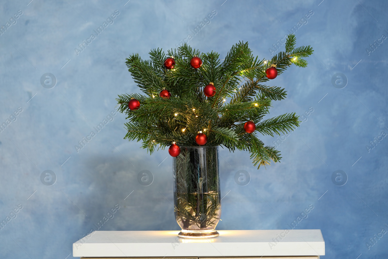 Photo of Beautiful decorated fir tree branches on white table near blue wall. Christmas season