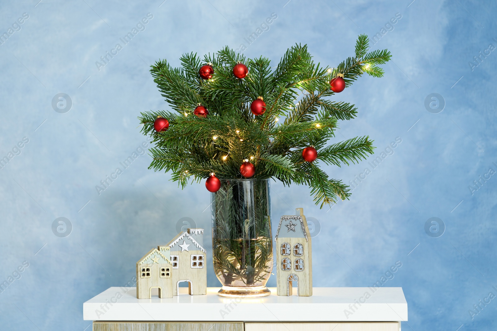 Photo of Beautiful decorated fir tree branches on white table near blue wall. Christmas season