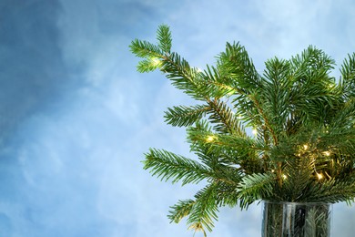 Photo of Beautiful fir tree branches decorated with Christmas lights on blue background, closeup. Space for text