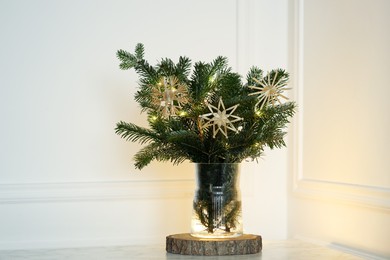 Photo of Beautiful decorated fir tree branches on table near white wall. Christmas season