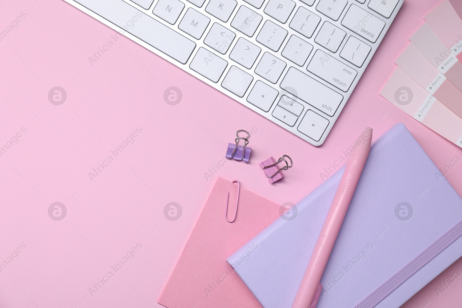 Photo of Designer's workplace with keyboard and stationery on pink background, flat lay. Space for text