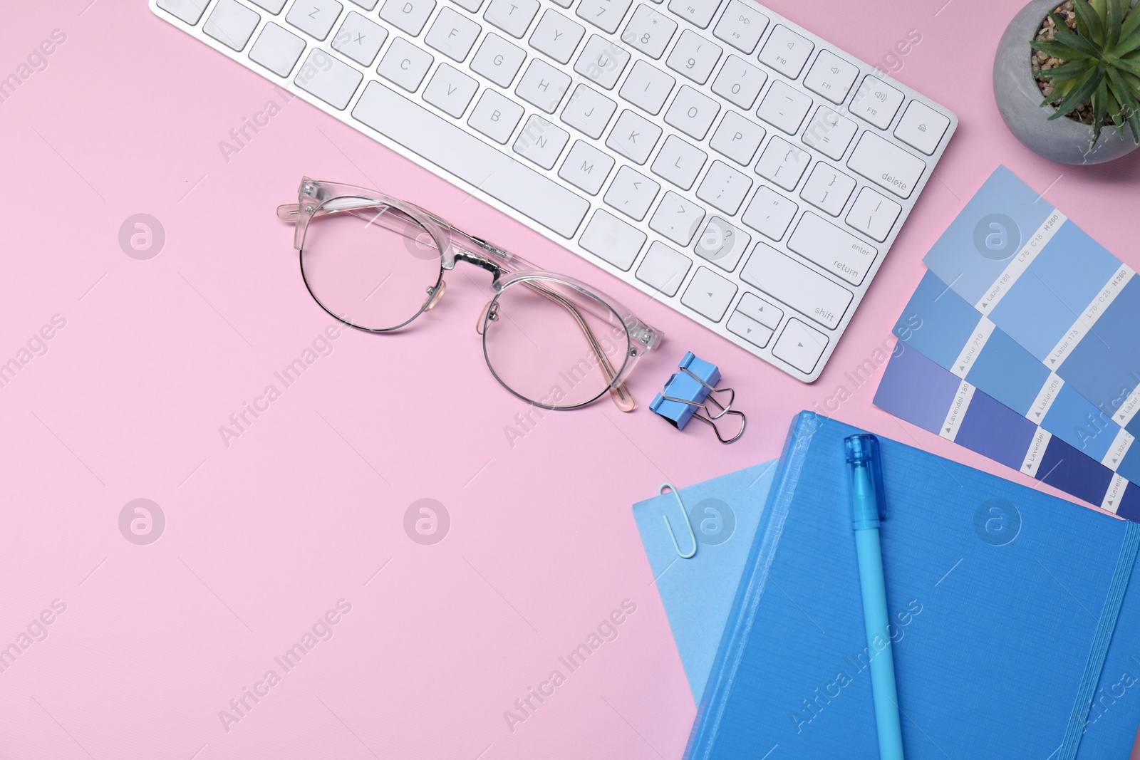 Photo of Designer's workplace with keyboard and stationery on pink background, flat lay. Space for text