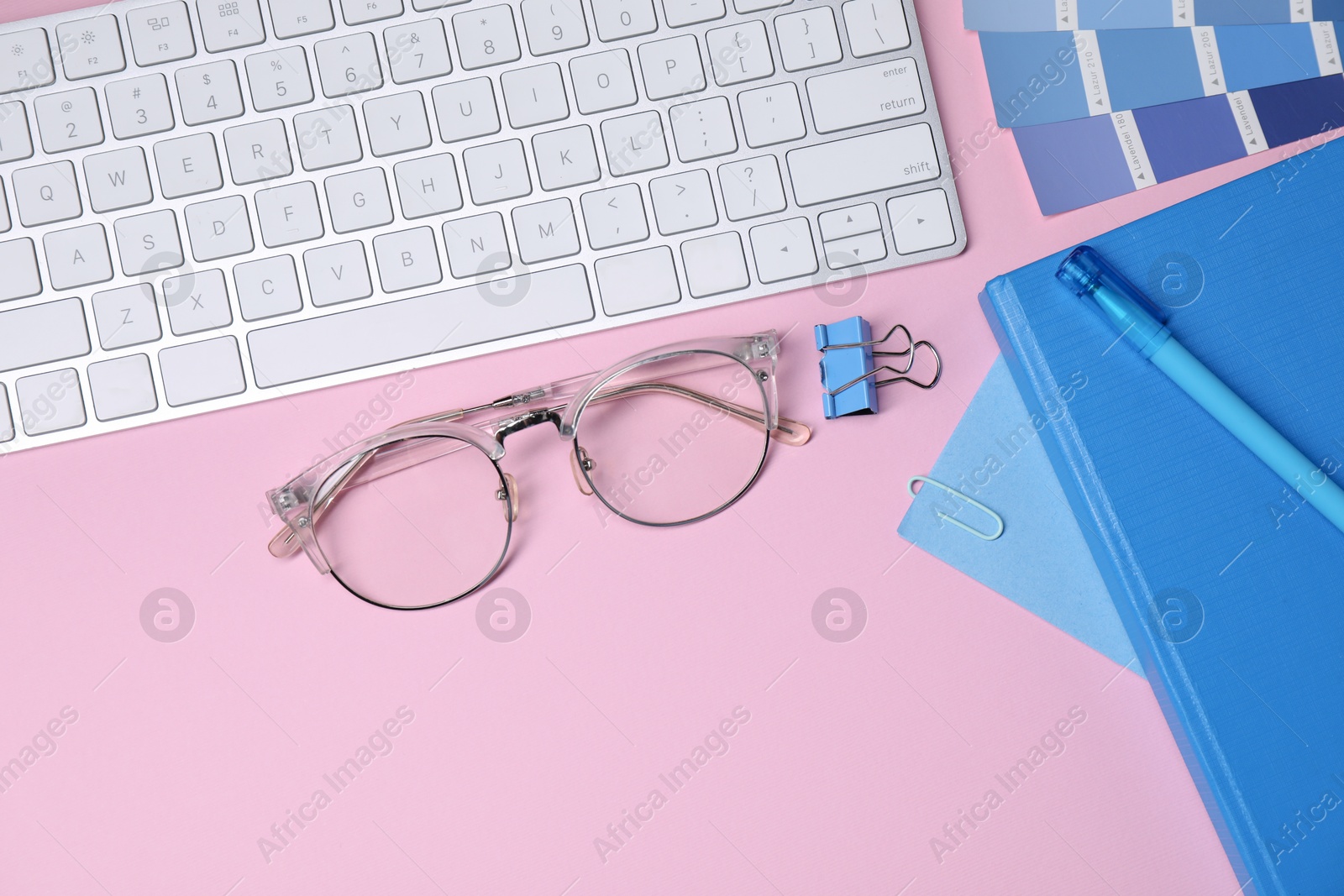 Photo of Designer's workplace with keyboard and stationery on pink background, flat lay. Space for text