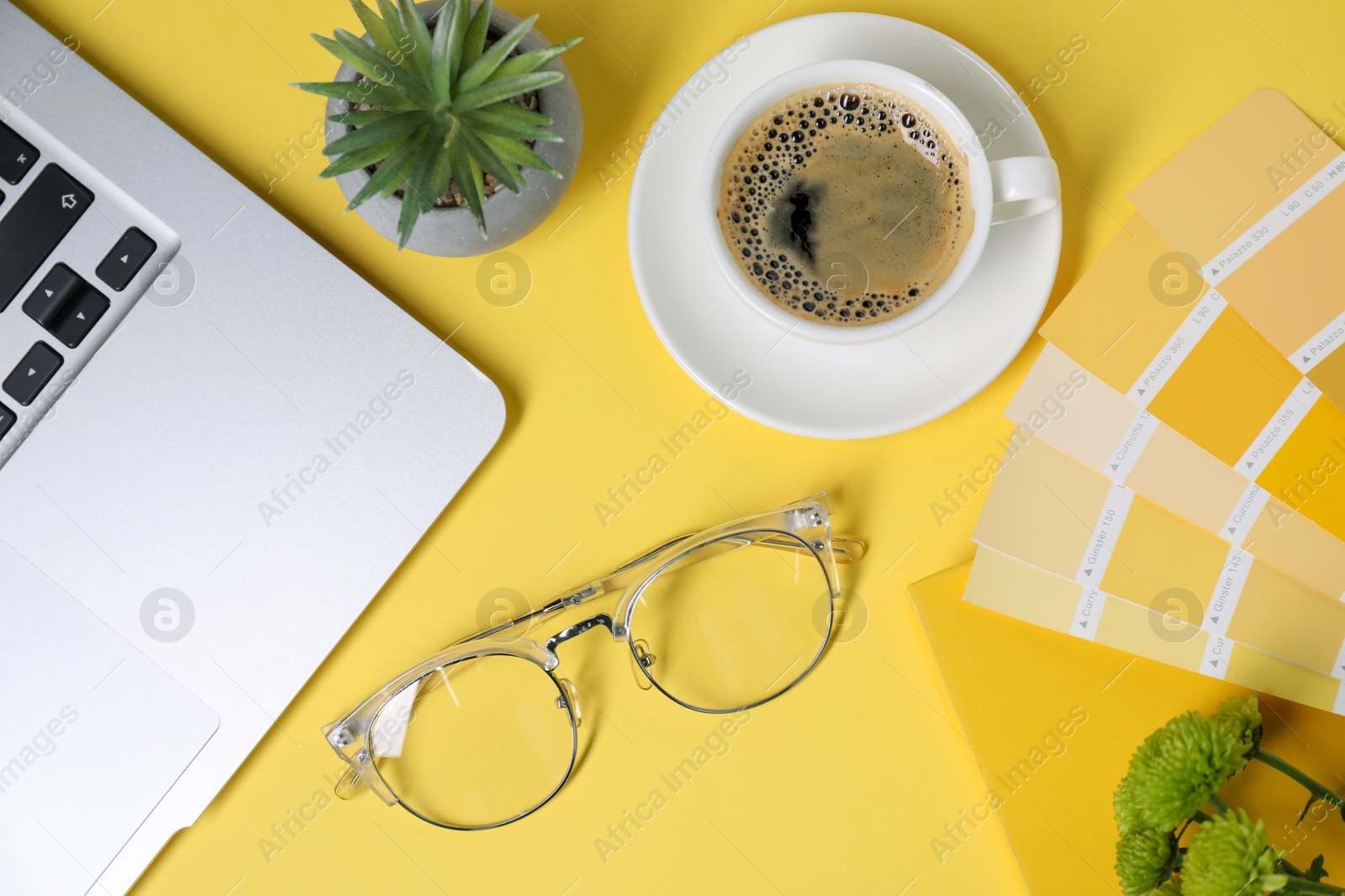 Photo of Designer's workplace with laptop, stationery and cup of coffee on yellow background, flat lay