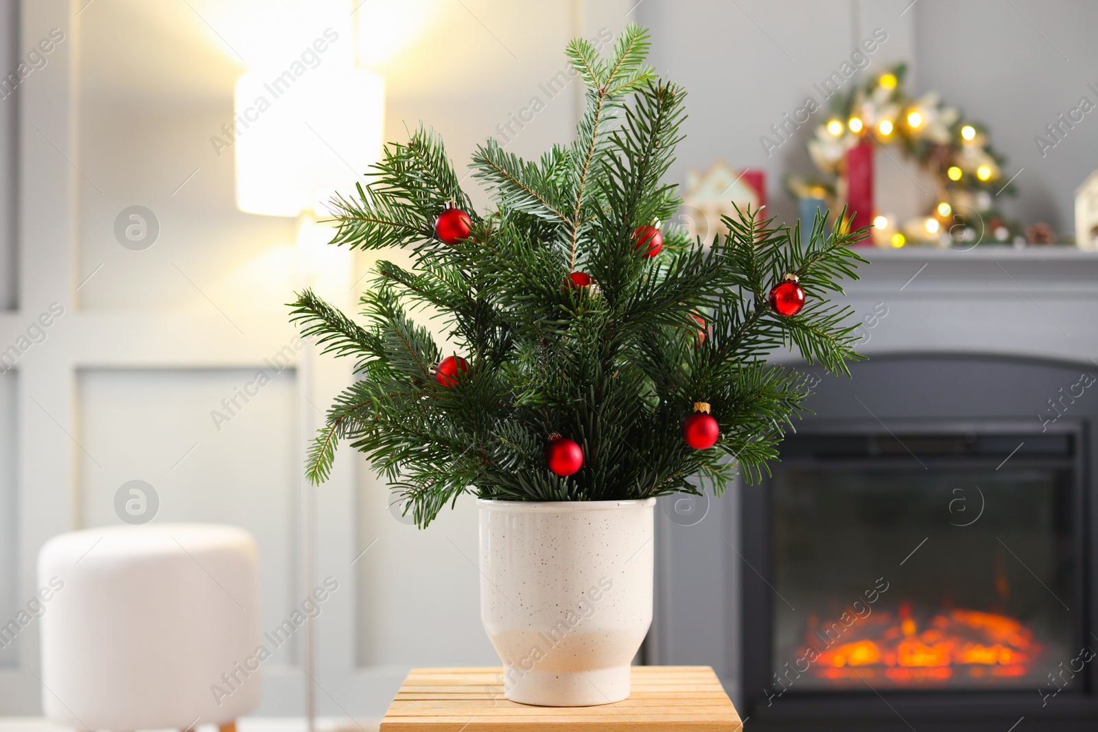 Photo of Beautiful Christmas composition of decorated fir tree branches on stool indoors