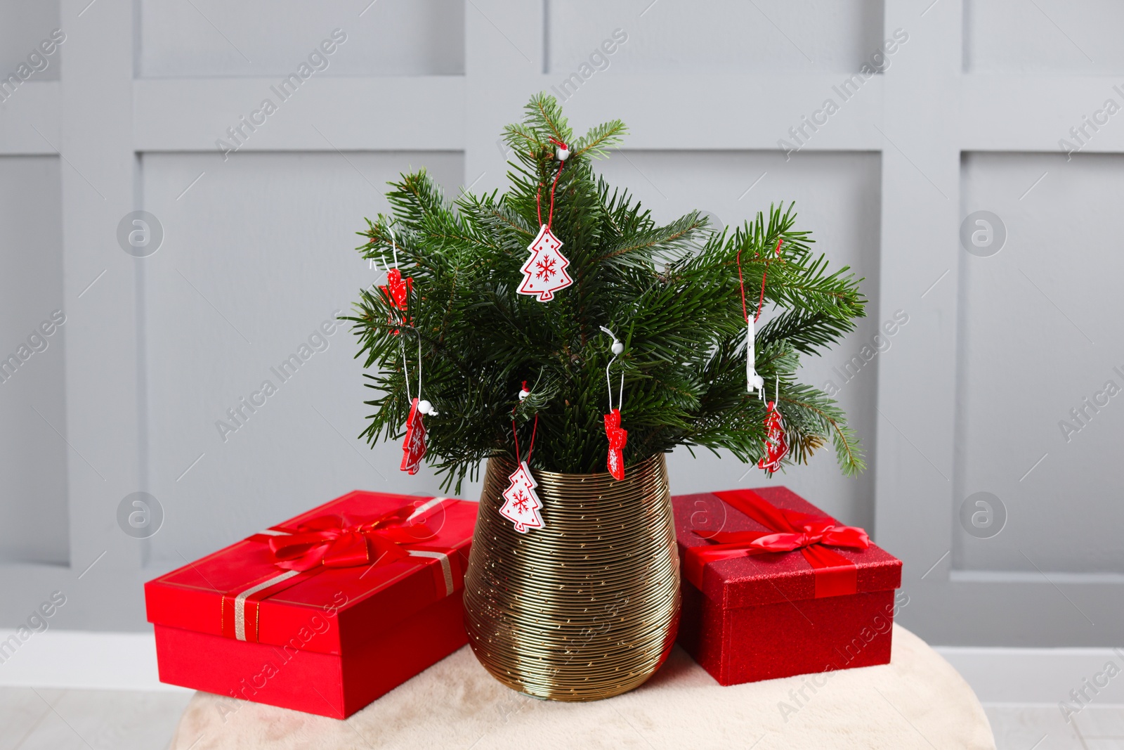 Photo of Beautiful decorated fir tree branches and Christmas gifts on pouf indoors