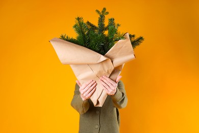 Photo of Woman with bouquet of fir branches on orange background. Christmas decor