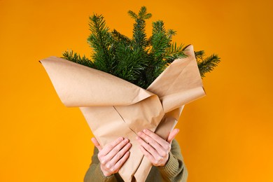 Photo of Woman with bouquet of fir branches on orange background. Christmas decor