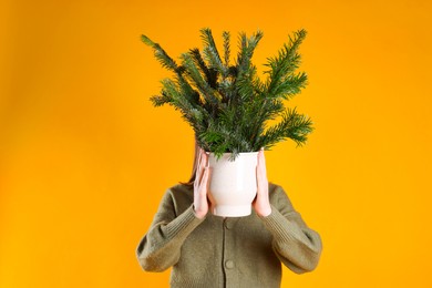 Photo of Woman with bouquet of fir branches on orange background. Christmas decor