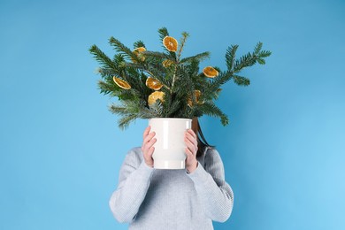 Photo of Woman holding beautiful Christmas composition of fir tree branches decorated with dried orange slices on blue background