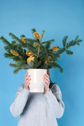 Photo of Woman holding beautiful Christmas composition of fir tree branches decorated with dried orange slices on blue background