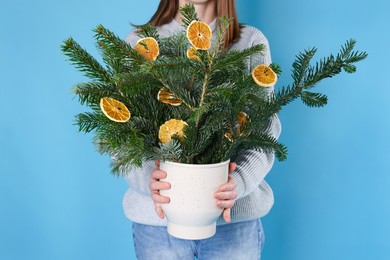 Photo of Woman holding beautiful Christmas composition of fir tree branches decorated with dried orange slices on blue background, closeup