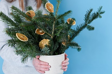 Photo of Woman holding beautiful Christmas composition of fir tree branches decorated with dried orange slices on blue background, closeup