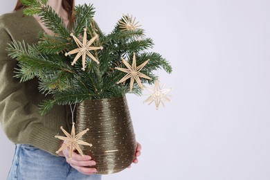 Photo of Woman holding beautiful Christmas composition of decorated fir tree branches on light background, closeup. Space for text