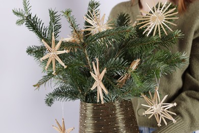 Photo of Woman holding beautiful Christmas composition of decorated fir tree branches on light background, closeup