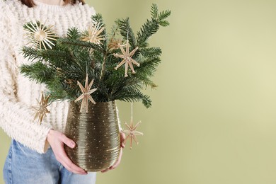 Photo of Woman holding beautiful Christmas composition of decorated fir tree branches on light green background, closeup. Space for text