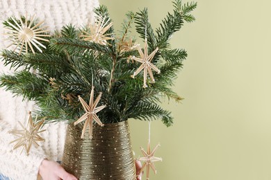 Photo of Woman holding beautiful Christmas composition of decorated fir tree branches on light green background, closeup. Space for text