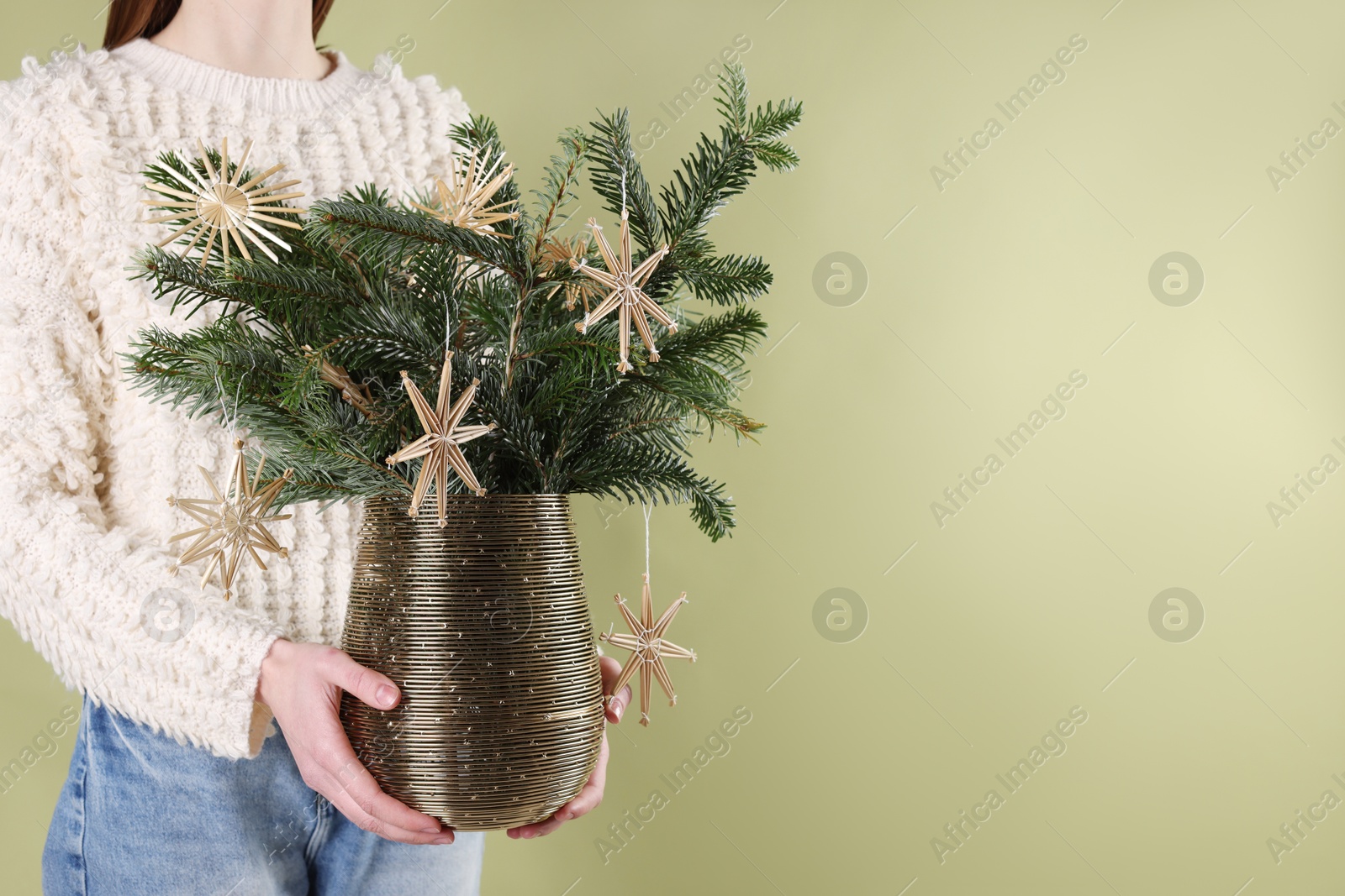 Photo of Woman holding beautiful Christmas composition of decorated fir tree branches on light green background, closeup. Space for text