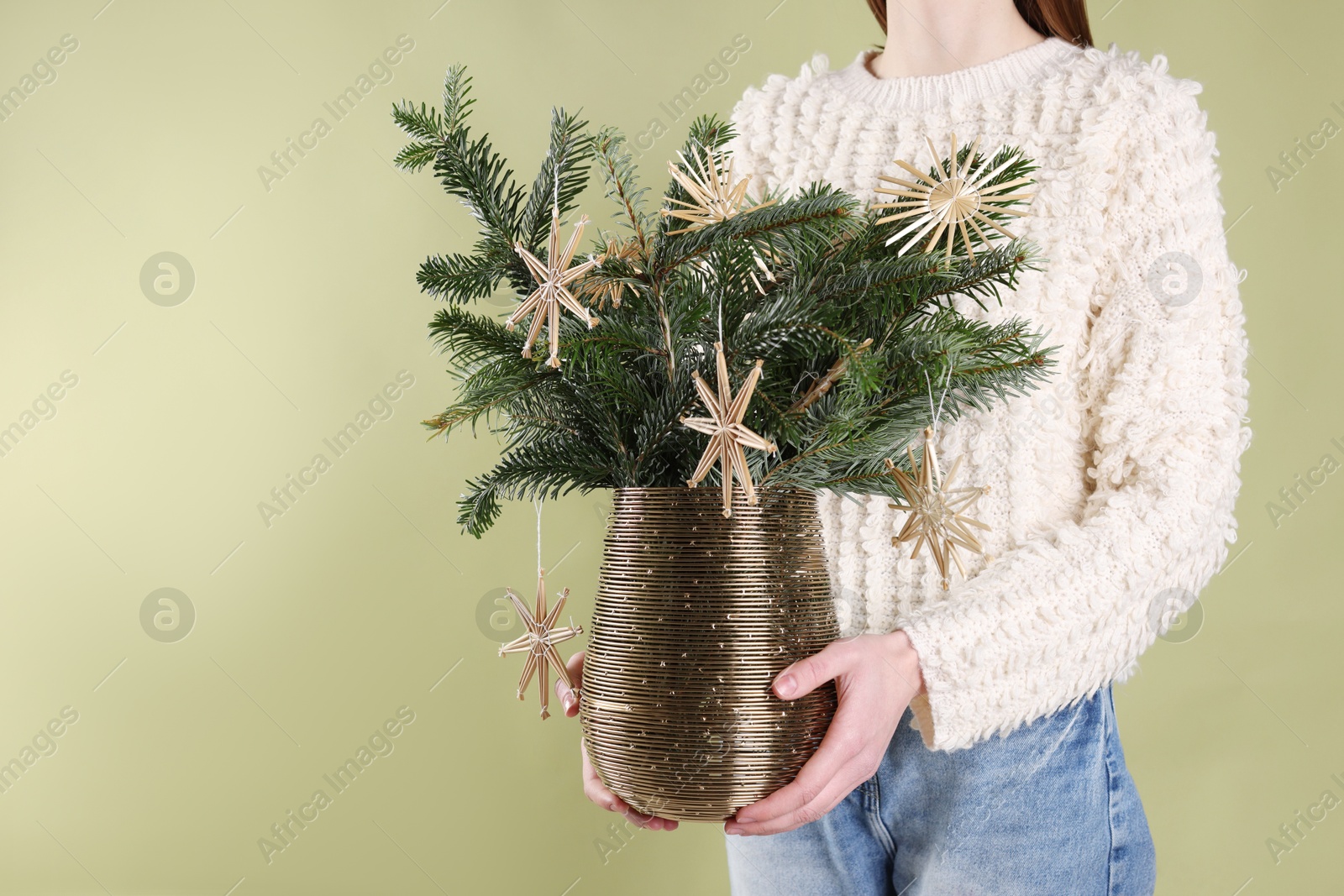 Photo of Woman holding beautiful Christmas composition of decorated fir tree branches on light green background, closeup. Space for text