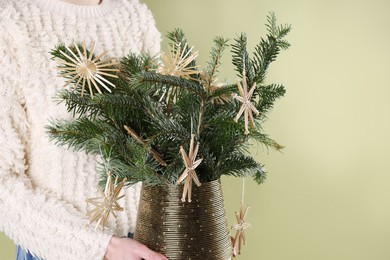 Photo of Woman holding beautiful Christmas composition of decorated fir tree branches on light green background, closeup