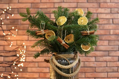 Photo of Beautiful fir tree branches decorated with dried orange slices and cinnamon sticks in vase against Christmas lights