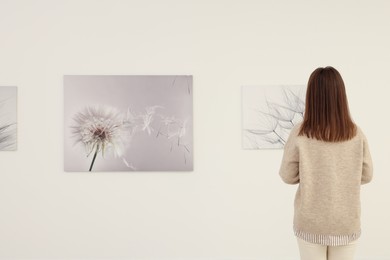 Photo of Woman studying beautiful artwork in modern gallery, back view