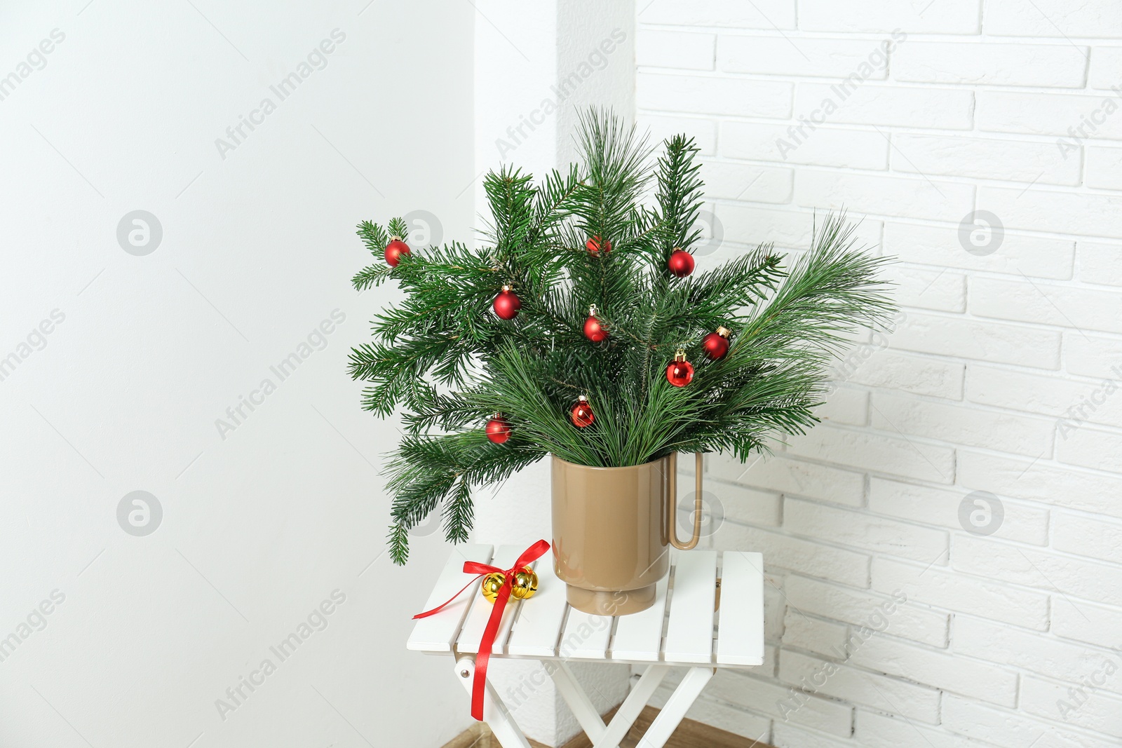 Photo of Beautiful Christmas composition of decorated fir and pine tree branches on stool at home