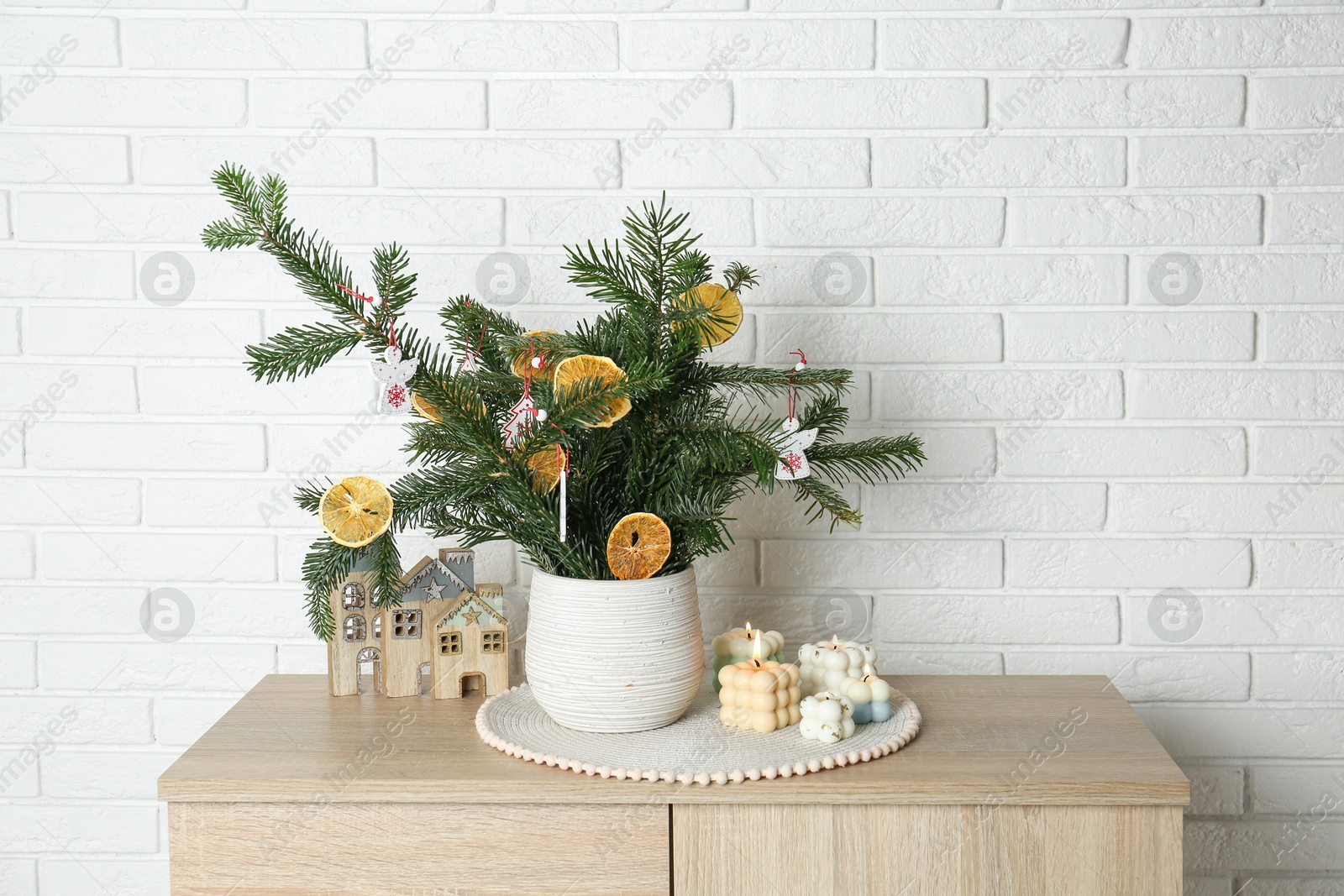 Photo of Beautiful Christmas composition of decorated fir tree branches on wooden nightstand near white brick wall