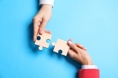 Photo of Business strategy and teamwork concept. Partners putting puzzle pieces together on light blue background, top view