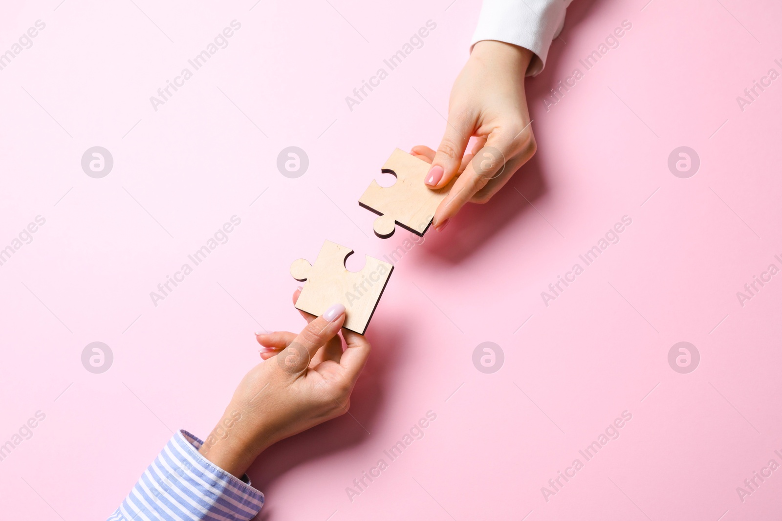 Photo of Business strategy and teamwork concept. Partners putting puzzle pieces together on pink background, top view