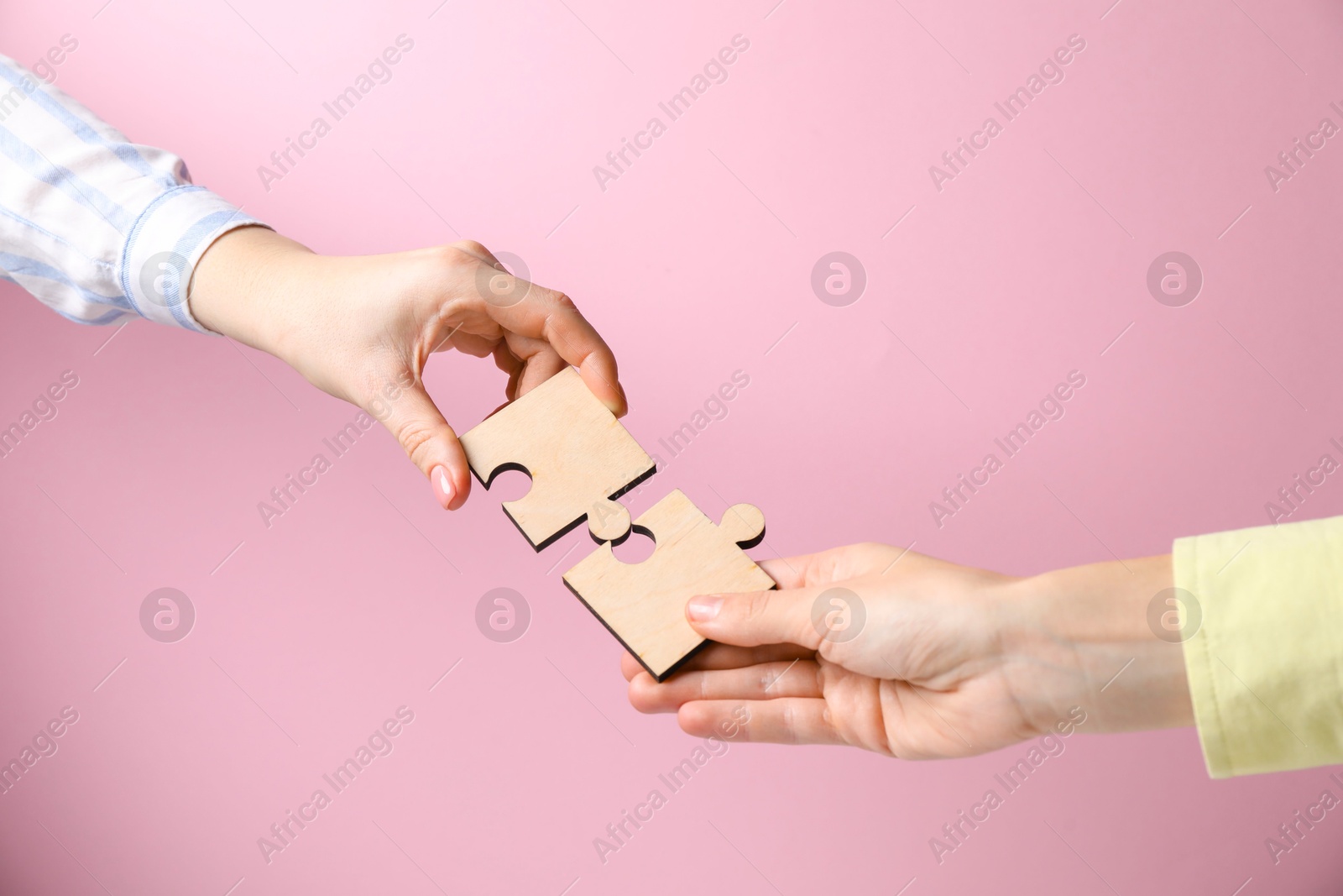 Photo of Business strategy and teamwork concept. Partners putting puzzle pieces together on pink background, closeup